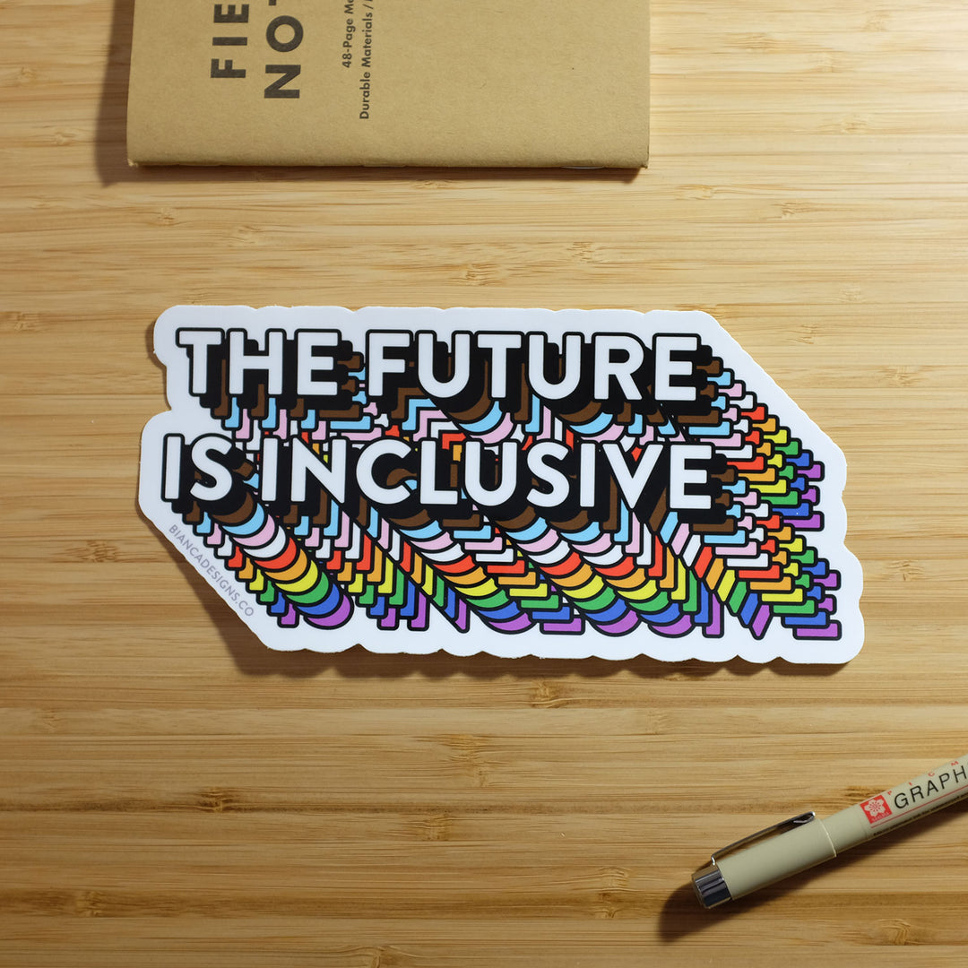 The Future Is Inclusive Bumper Rainbow Sticker by Bianca Designs. The Sticker is placed by a small notebook and marker for scale.
