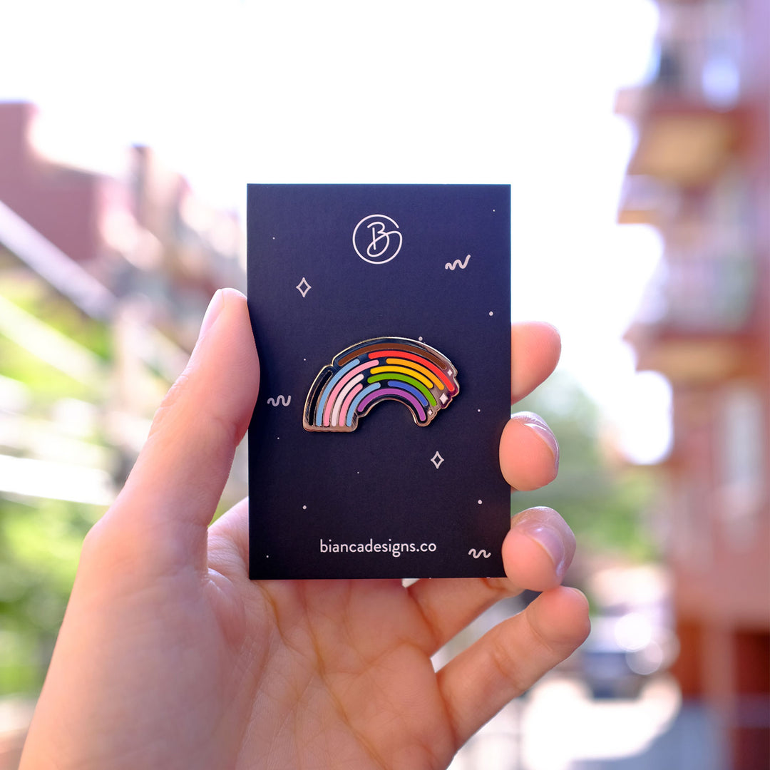 Hand holding the Inclusive Rainbow Pride Pin in Silver on a backing card by Bianca Designs