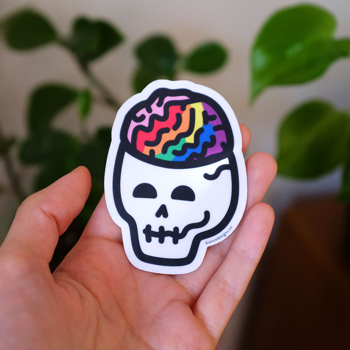 Hand holding the Queerie Queer Brain Skull Pride Sticker by Bianca Designs.