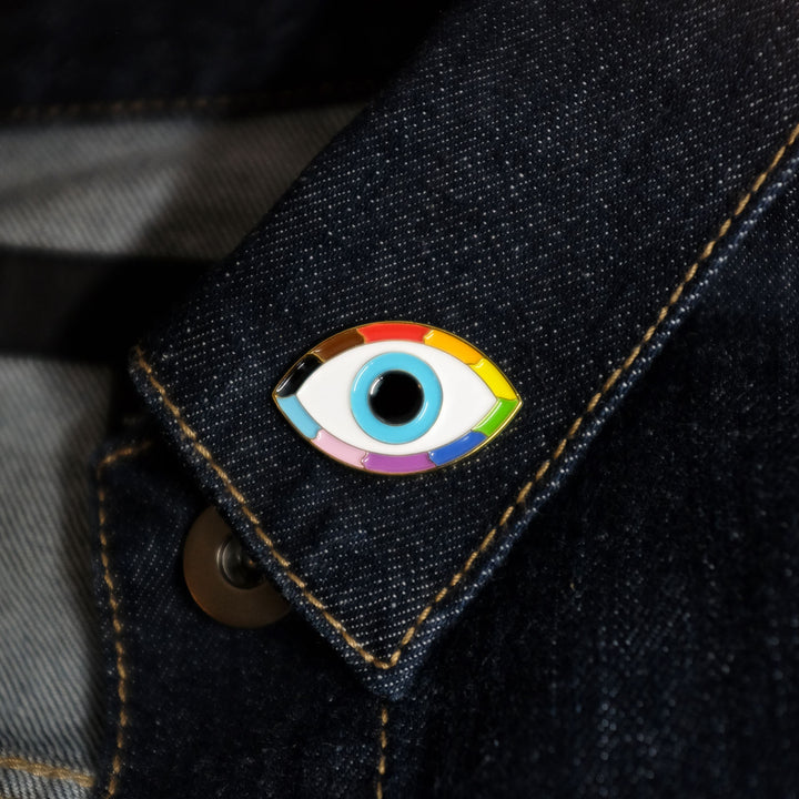 Queer Evil Eye Pride Enamel Pin by Bianca Designs. The pin is worn on a denim jackets collar.