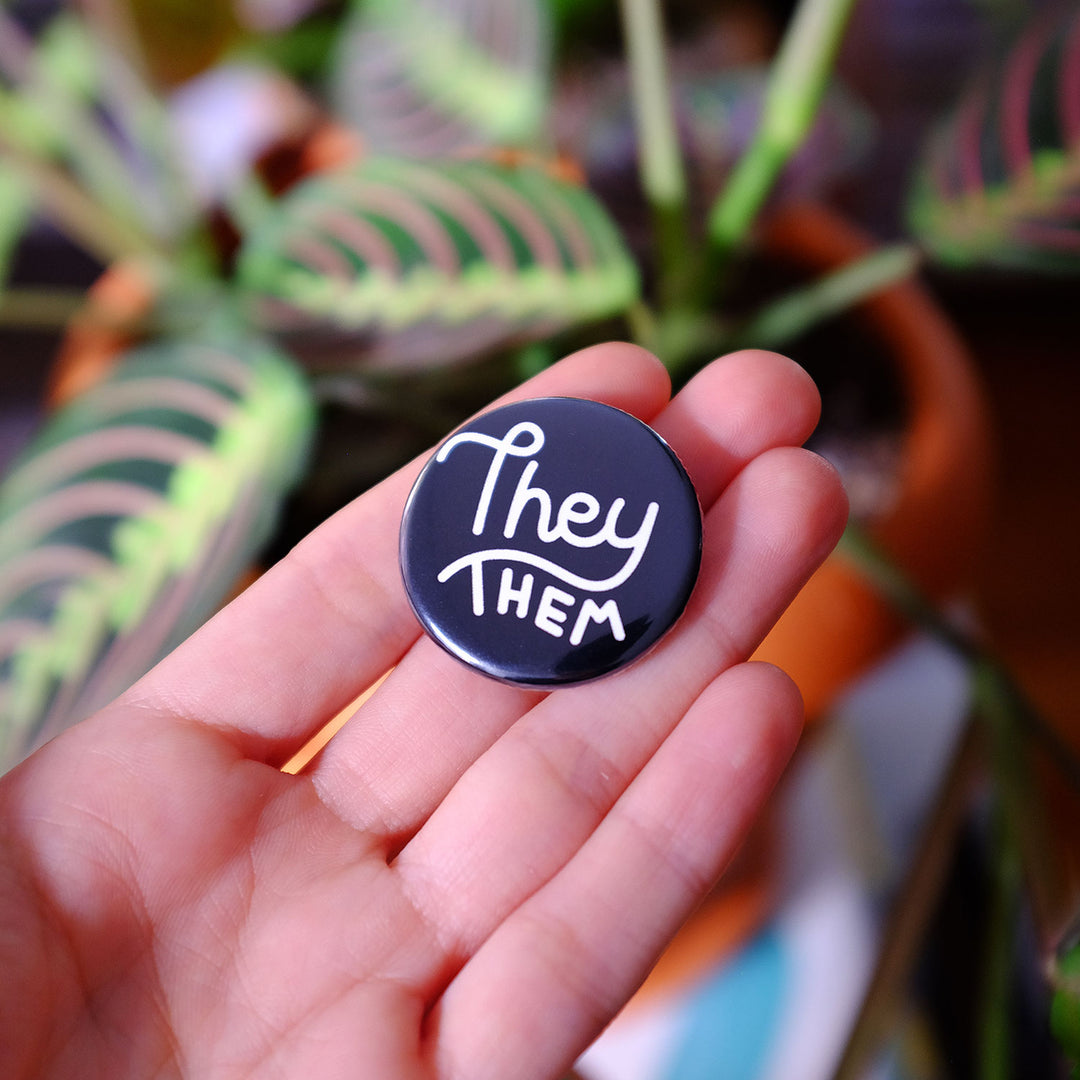 Hand holding the They/them Pronouns Button by Bianca Designs.