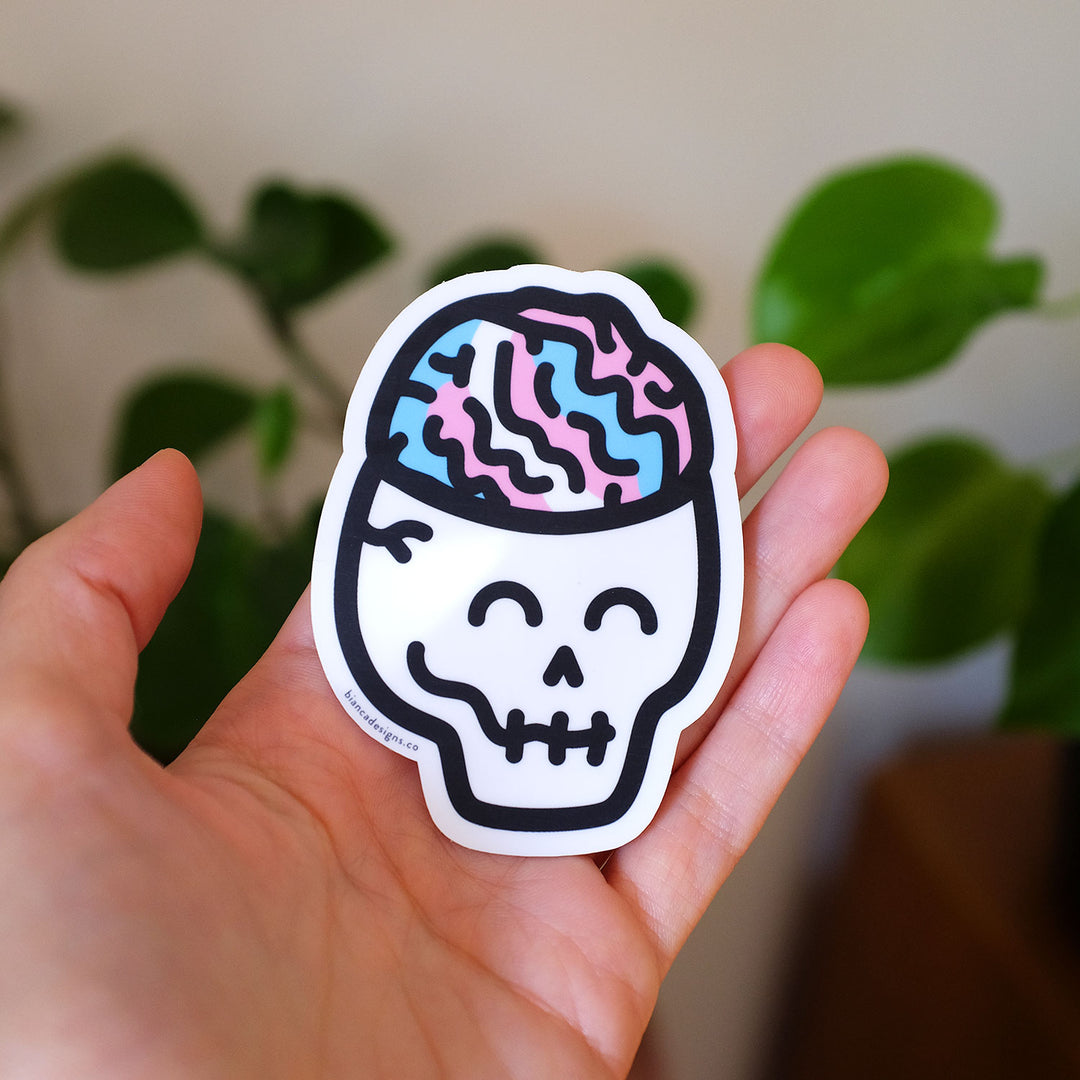 Hand holding the Eerie Trans Brain Skull Pride Sticker by Bianca Designs