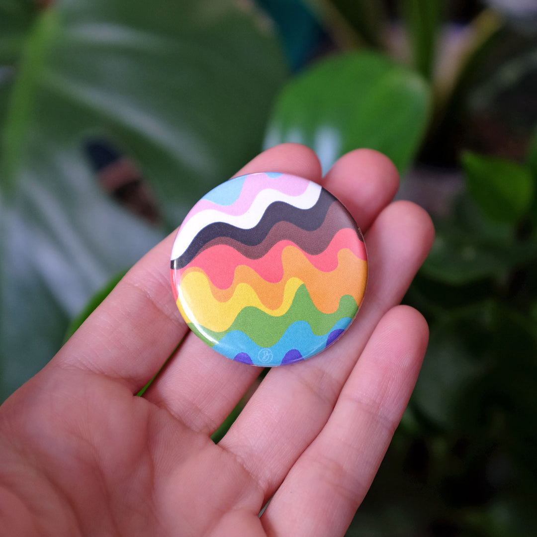 Hand holding the Wavy Inclusive Pride Rainbow Button by Bianca Designs.