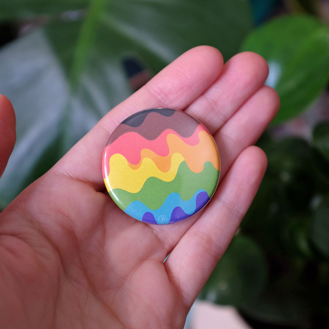 Hand holding the Wavy QTPOC Pride Rainbow Button by Bianca Designs.